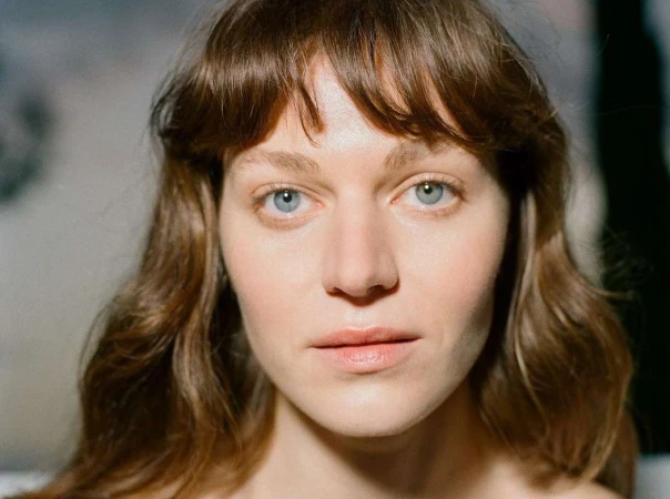 Close-up portrait of a woman with blue eyes, brown wavy hair with bangs, and neutral expression by Jessica Sidenros in Paris.