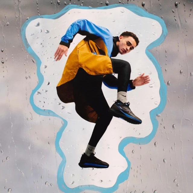 Athletic man in motion jumps against a cloudy backdrop with raindrop overlay, wearing running shoes, blue and yellow jacket, and black leggings.