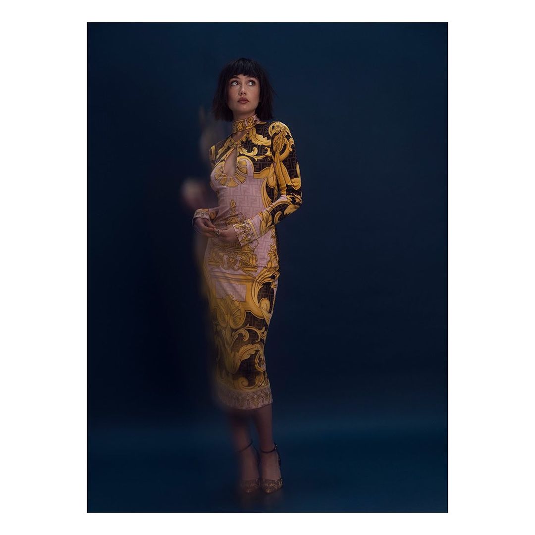 Elegant woman in patterned long-sleeve dress poses in front of a dark background. Fashion editorial shot with shallow depth of field.