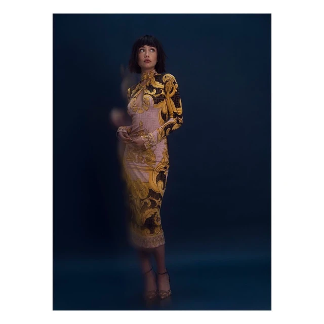 Elegant woman in patterned long-sleeve dress poses in front of a dark background. Fashion editorial shot with shallow depth of field.