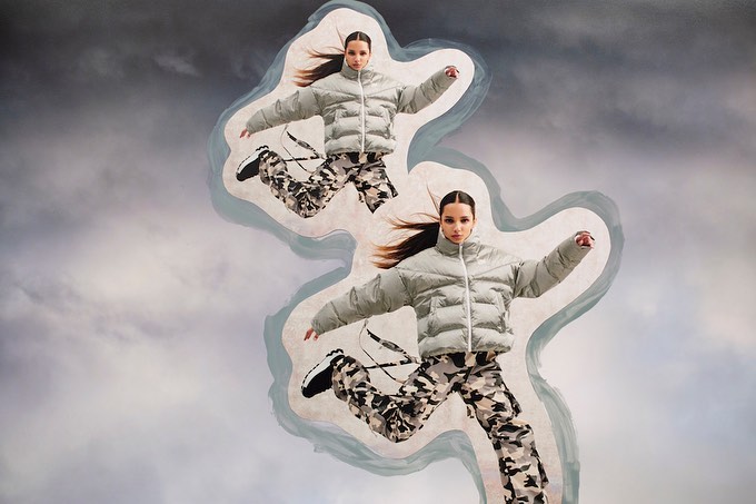 Two women in puffer jackets and camouflage pants are jumping against a cloudy sky in a collage. Fashion and editorial style.