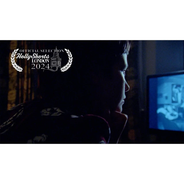 Close-up of a young boy looking at a screen indoors in a dimly lit room, overlaid with a film festival logo, in a dark setting.