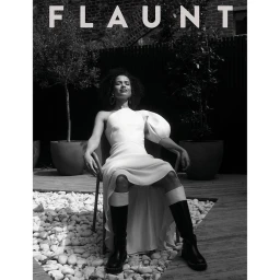 Black and white portrait of a woman in a white dress and black boots seated in a courtyard by photographer Jessie Craig.