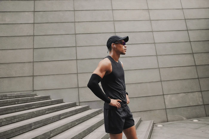Athletic man wearing a black athletic tank top, cap, and sunglasses standing on outdoor stone steps in London
