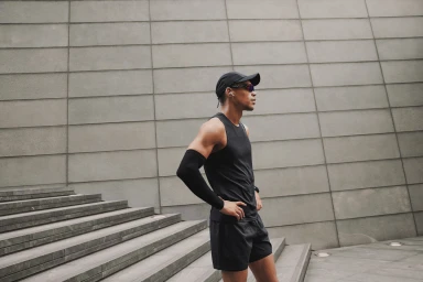 Athletic man wearing a black athletic tank top, cap, and sunglasses standing on outdoor stone steps in London