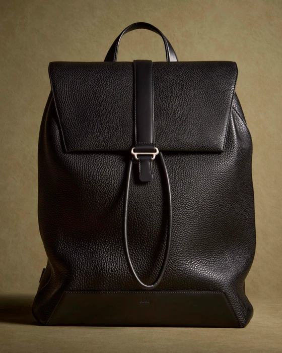 Black pebbled leather luxury backpack with a top flap closure and central strap against an olive textured background.
