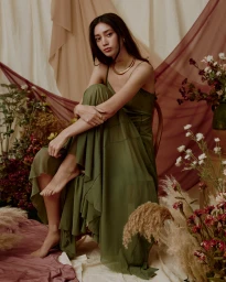 Woman in an olive green dress seated amidst draped fabrics and floral arrangements styled by Antonia Barath.