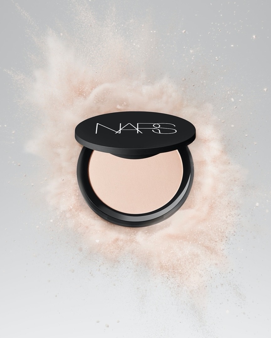 NARS powder compact on light grey backdrop with pink powder explosion, beauty photography for cosmetics advertising and product display.