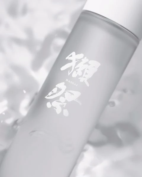 A bottle of Dassai sake is displayed against a blurred background with subtle textures and a minimalist aesthetic in a soft, diffused light.