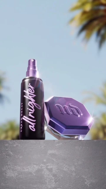 Urban Decay All Nighter setting spray and makeup compact displayed on a concrete surface against a bright blue sky with palm trees.