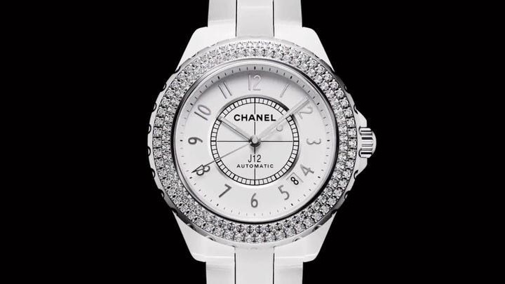 Close-up of a white Chanel J12 Automatic watch with a diamond-encrusted bezel and a white dial on a black background.