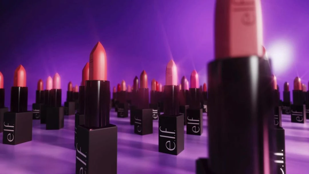 Multiple pink and black lipsticks with the e.l.f. logo are arranged in a row, in a purple-toned studio setting with soft lighting.