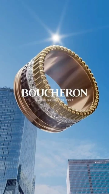 High-angle view of a gold Boucheron ring floating in front of modern buildings set against a bright blue sky and sunshine.