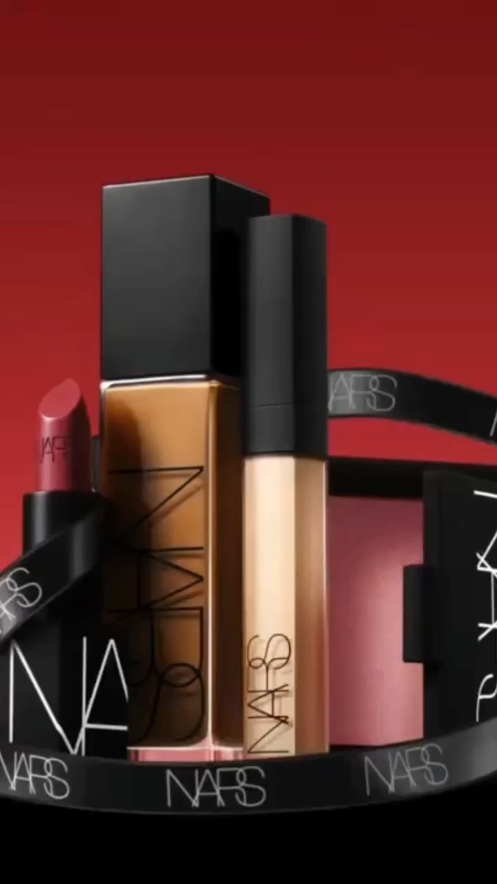 NARS makeup set including foundation, concealer, lipstick, and blush compact arranged on a red backdrop with NARS-branded ribbon.