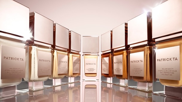Several Patrick TA foundation bottles are arranged in a row, featuring clear glass containers and reflective white caps, evenly spaced.