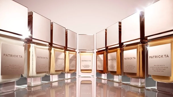 Several Patrick TA foundation bottles are arranged in a row, featuring clear glass containers and reflective white caps, evenly spaced.