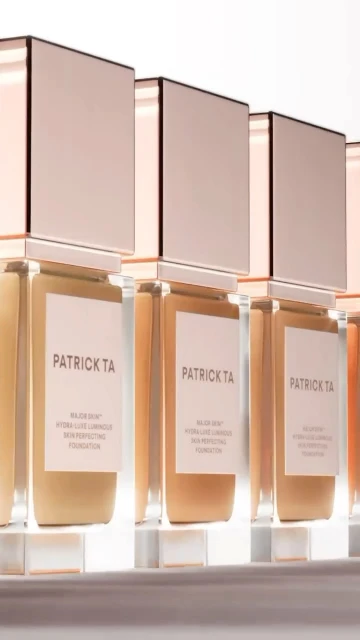 Cosmetic product display featuring several Patrick TA Major Skin hydra-silk non-perfecting foundation bottles lined up, beauty advertisement.