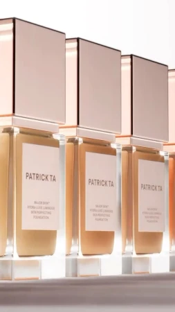 Cosmetic product display featuring several Patrick TA Major Skin hydra-silk non-perfecting foundation bottles lined up, beauty advertisement.
