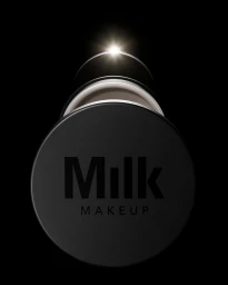Close-up product shot of a black cosmetic jar featuring the Milk Makeup logo against a dark background with a bright light gleam.