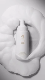 White skincare bottle nestled within swirling foam peaks against a textured background