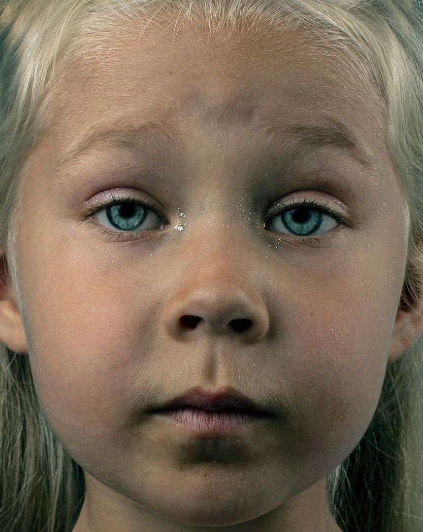 Close-up portrait of a young blond child with striking blue eyes and subtle glitter on skin by Jet Swan