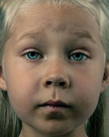 Close-up portrait of a young blond child with striking blue eyes and subtle glitter on skin by Jet Swan