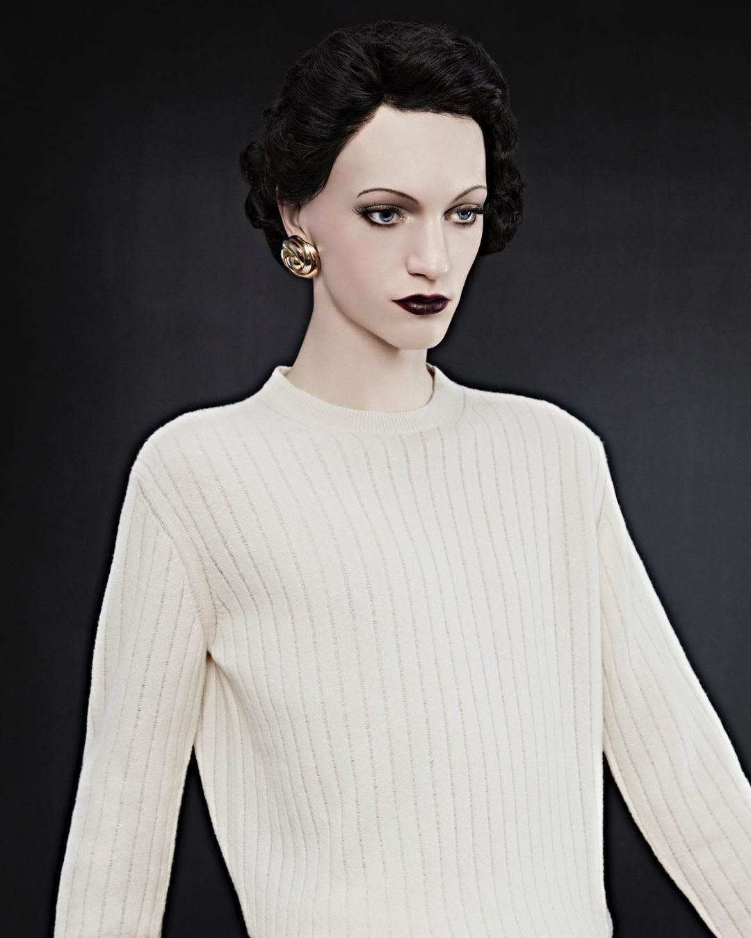 Mannequin in a cream-colored ribbed sweater with gold earrings against a dark background, fashion-forward and ready for retail display.