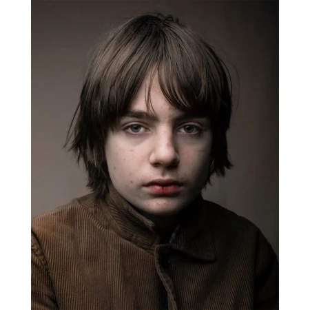 Portrait of a young boy with brown hair and eyes wearing a corduroy jacket in front of a neutral studio background, eye-level shot.