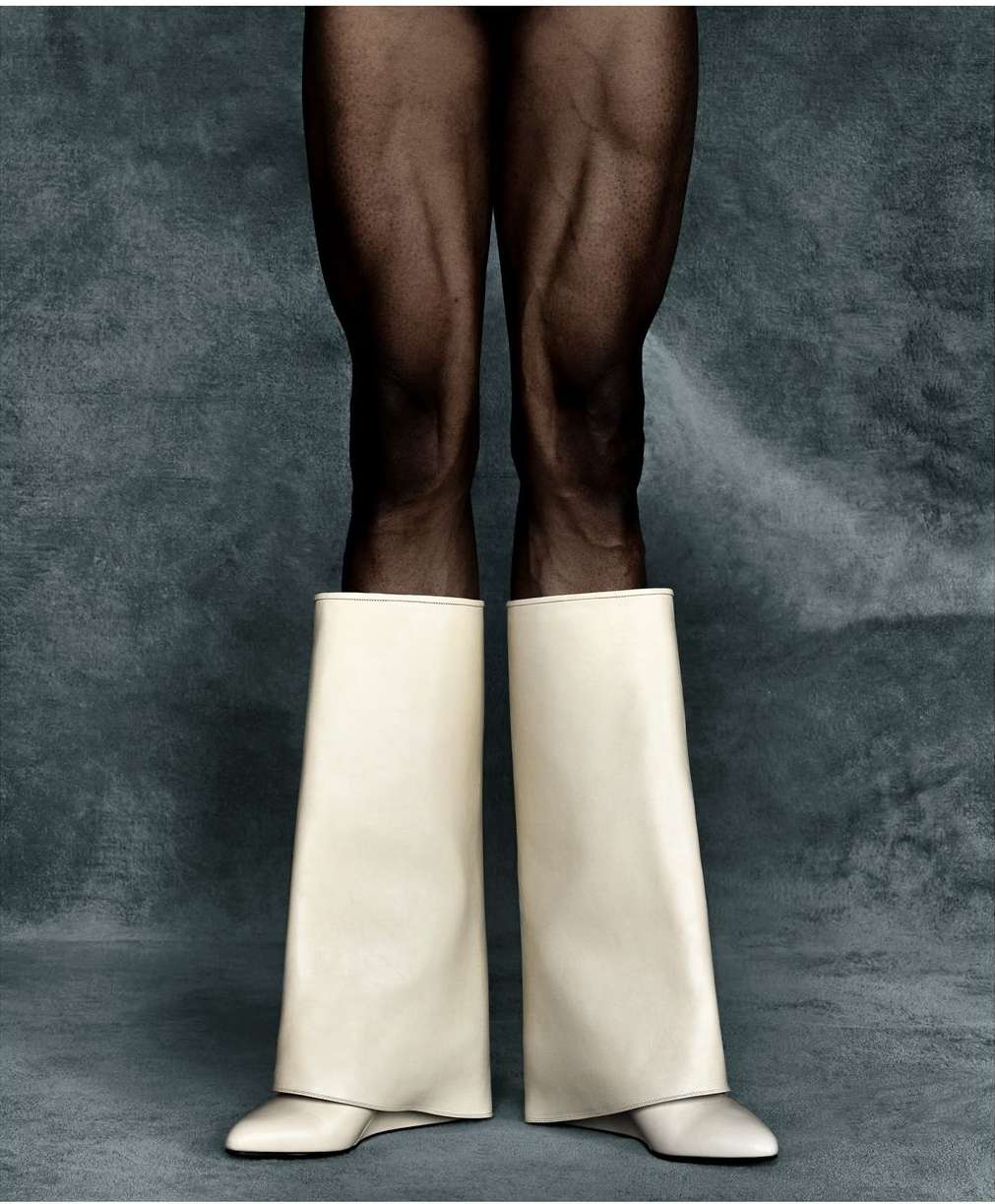 Legs with black tights and wide white boots against a muted grey-blue backdrop, studio lighting with neutral tones, clean fashion shot.