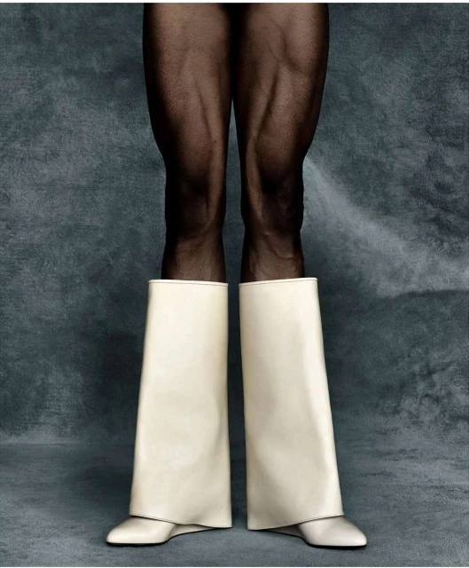 Legs with black tights and wide white boots against a muted grey-blue backdrop, studio lighting with neutral tones, clean fashion shot.
