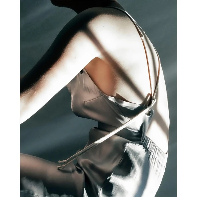 An adult female with a fair complexion is shown in a studio setting wearing a light silver sleeveless top with thin straps and loose pants.