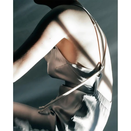 An adult female with a fair complexion is shown in a studio setting wearing a light silver sleeveless top with thin straps and loose pants.