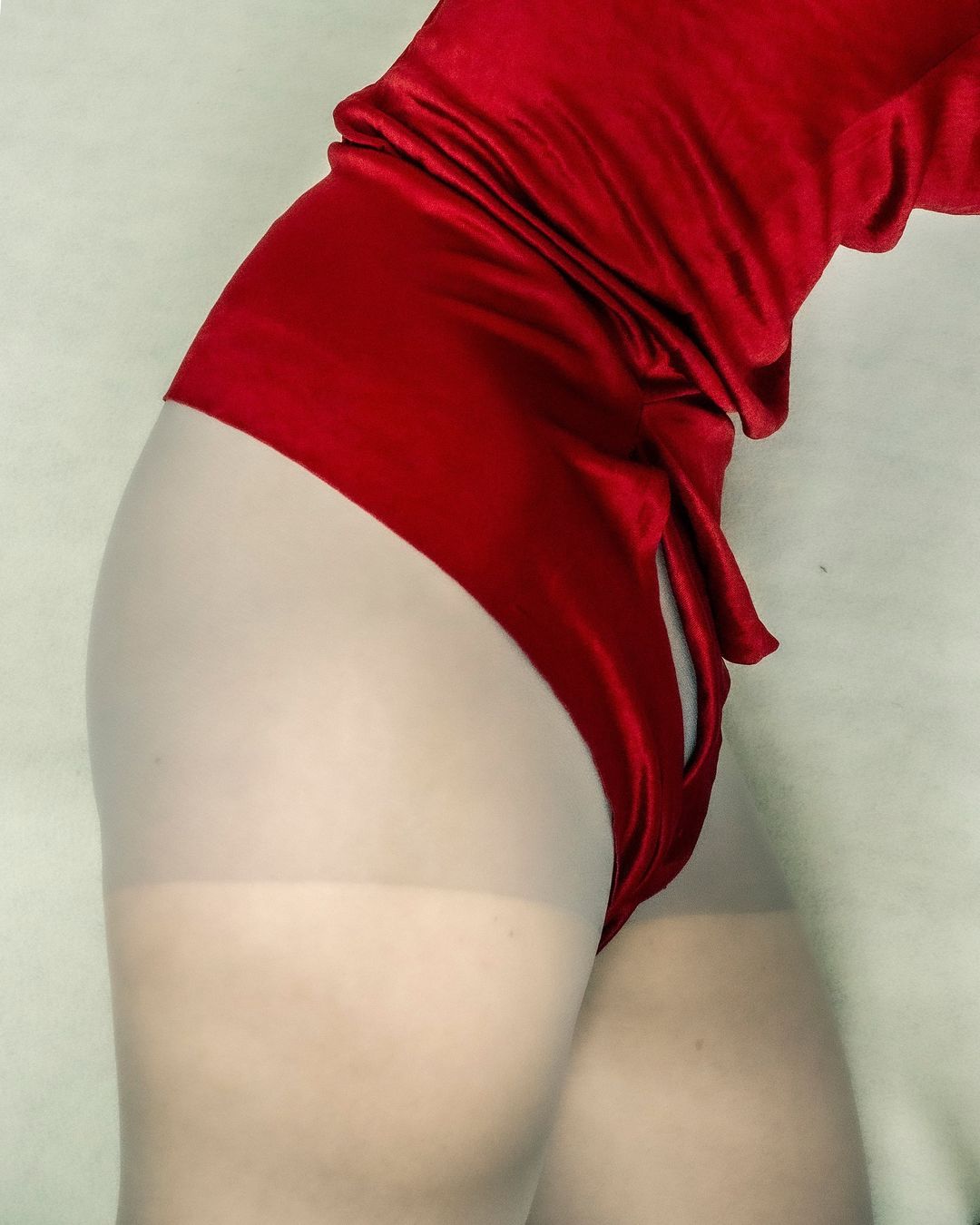Close-up studio shot of a person wearing a red velvet leotard and sheer tights, showcasing fashion and body contour.