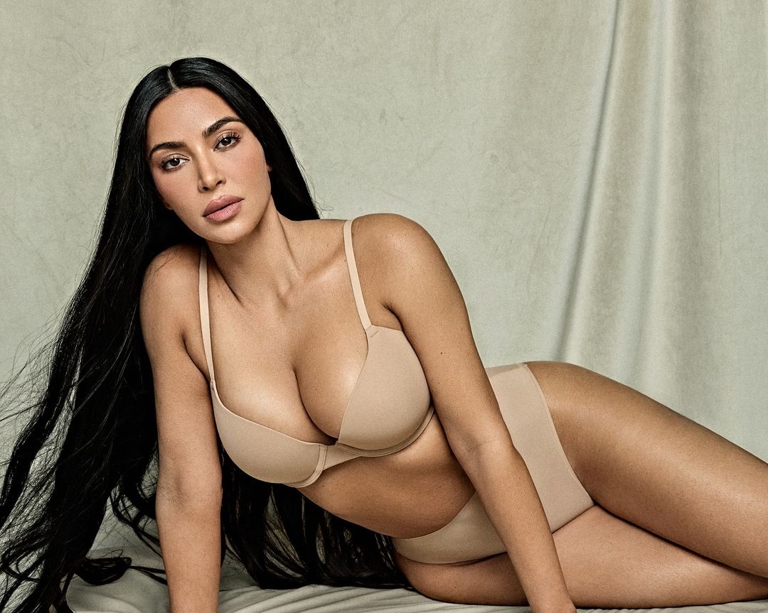 Adult woman in lingerie poses in a studio. The photo features a female adult lying down with long dark hair and neutral skin tone.