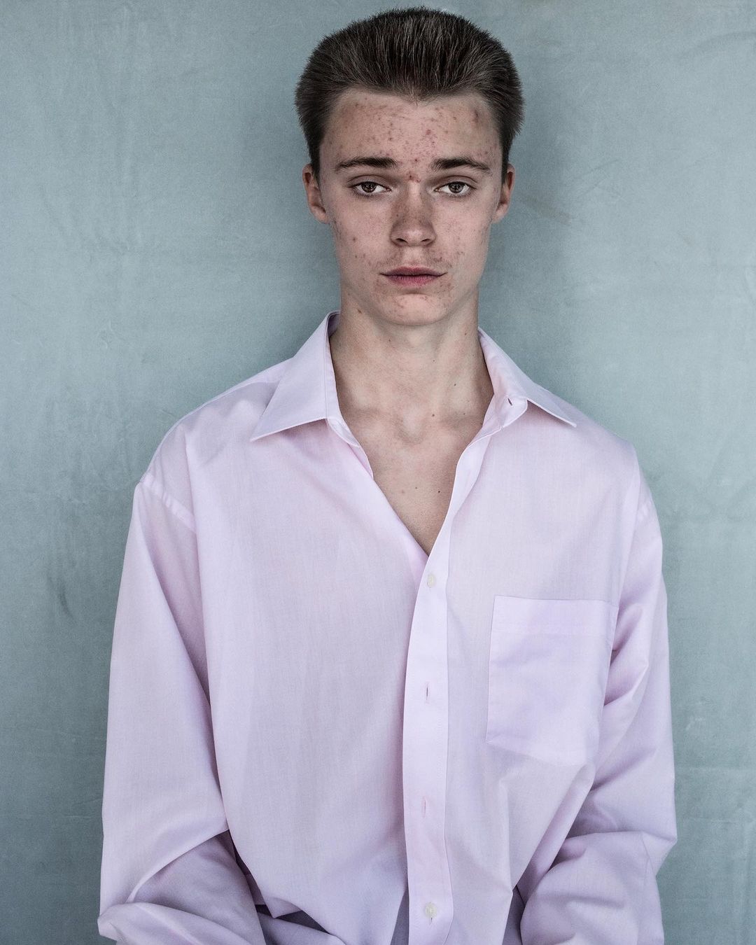 Portrait of a young man wearing a light pink button-down shirt against a textured grey background by Jet Swan.