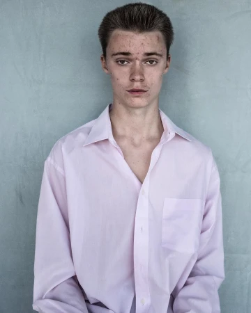 Portrait of a young man wearing a light pink button-down shirt against a textured grey background by Jet Swan.
