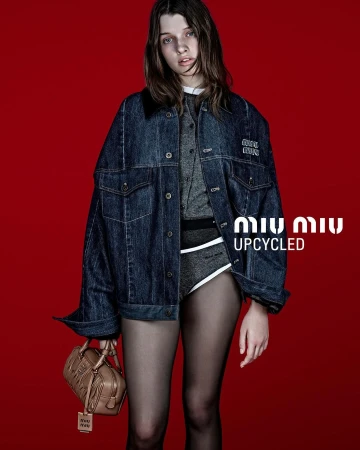 Model wearing an oversized denim jacket and carrying a brown leather handbag against a solid red background