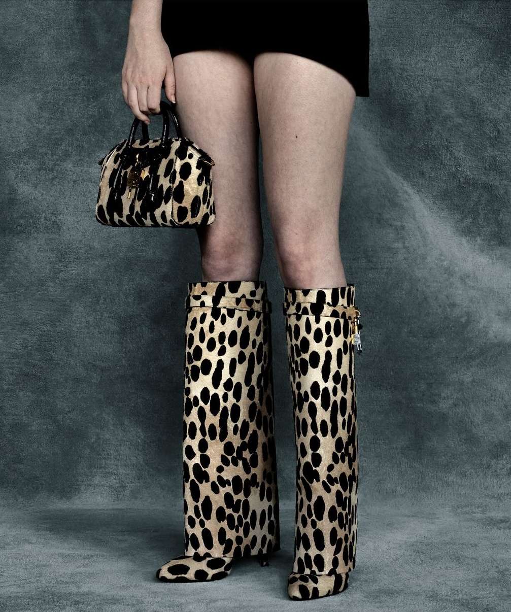 Woman wearing leopard print boots and carrying matching handbag against a grey background. Fashion shoot.