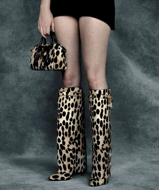 Woman wearing leopard print boots and carrying matching handbag against a grey background. Fashion shoot.