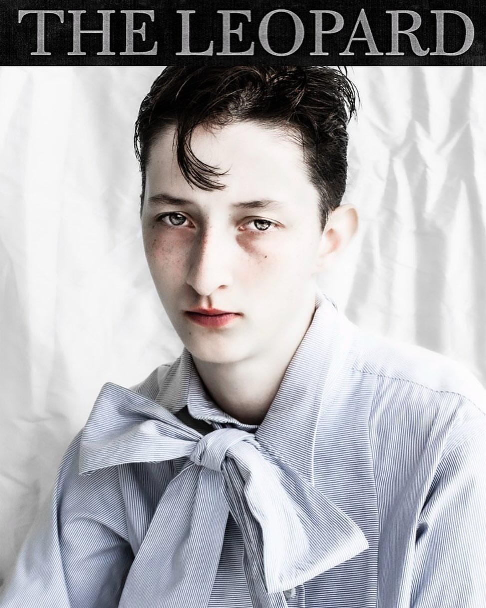 Close-up studio shot of a young adult with slicked-back dark hair wearing a light blue striped shirt and bow tie against a white backdrop.