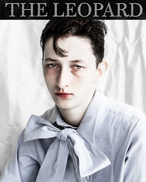 Close-up studio shot of a young adult with slicked-back dark hair wearing a light blue striped shirt and bow tie against a white backdrop.