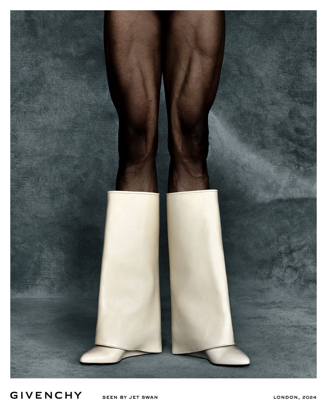 Fashion forward shot of model's legs in translucent tights and tall, wide, off-white boots on a grey textured background.