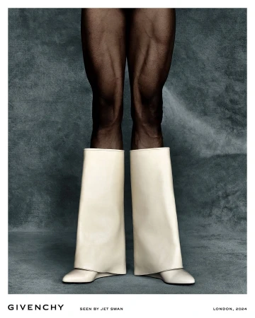 Close-up of muscular dark-skinned legs wearing wide cream-coloured leather boots against a textured grey background by Jet Swan