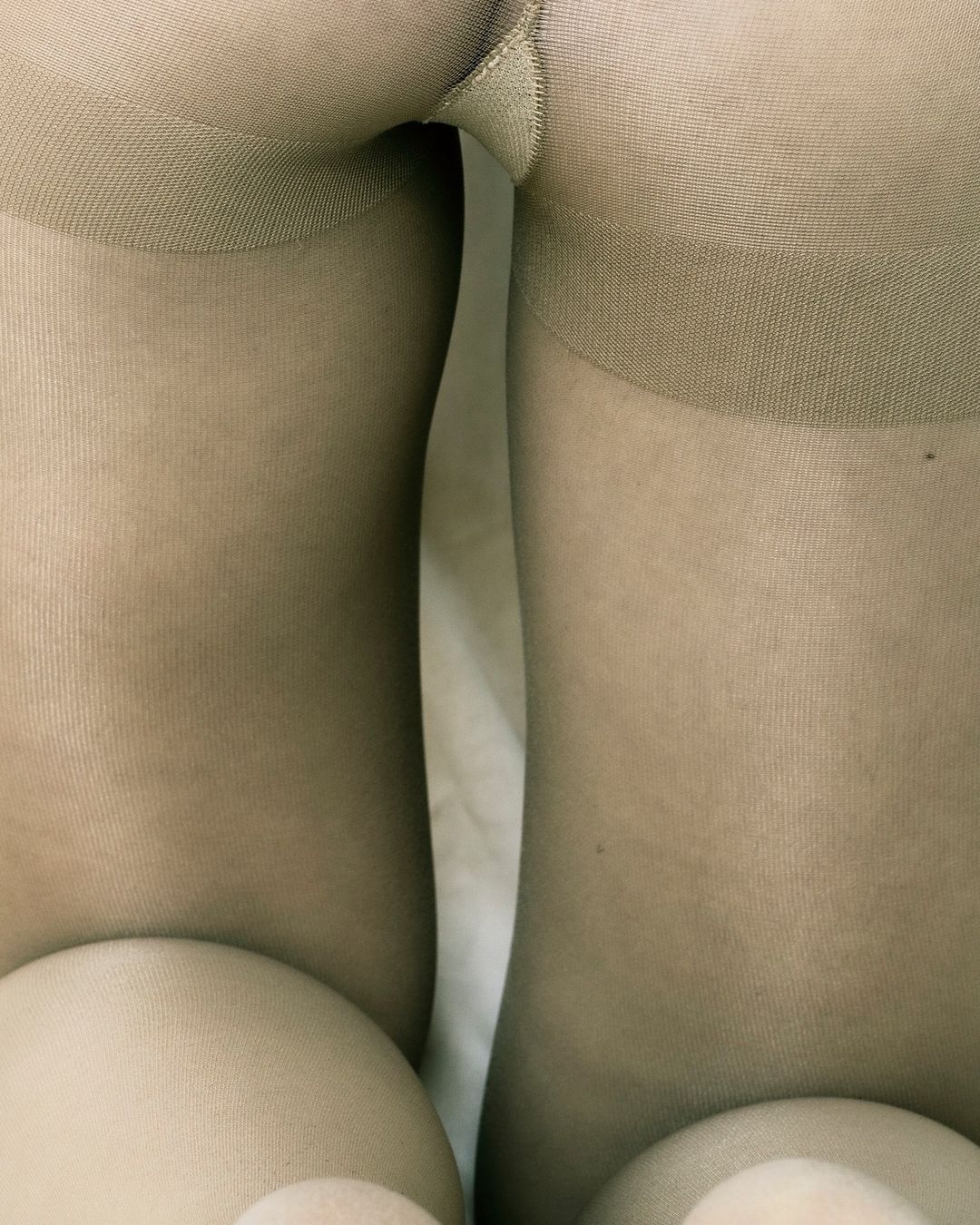 Close-up studio shot of woman's legs and torso in beige tights, highlighting texture and neutral tones against a plain background.