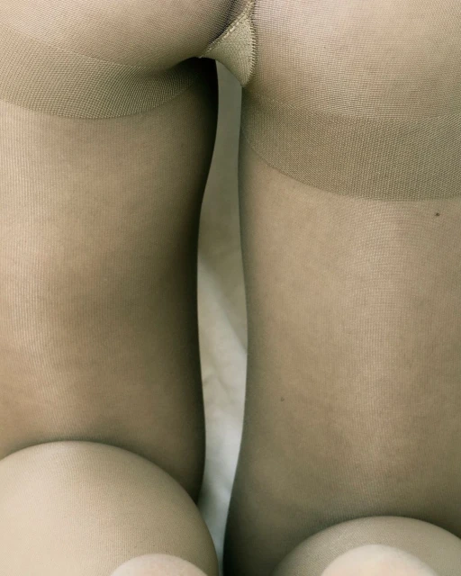 Close-up studio shot of woman's legs and torso in beige tights, highlighting texture and neutral tones against a plain background.