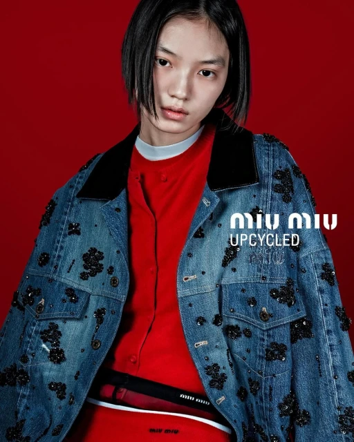 Fashion shot featuring a young adult female model wearing a denim jacket and a red top in front of a red backdrop.