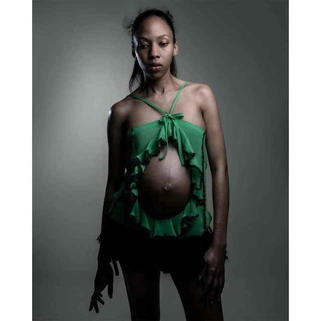 Portrait of pregnant woman in green top against gray background, showcasing maternity fashion and studio photography.