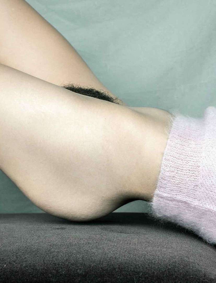 Closeup of person's lower legs and feet with pink socks resting on a dark grey surface against a light blue-grey backdrop.