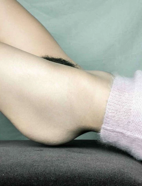 Closeup of person's lower legs and feet with pink socks resting on a dark grey surface against a light blue-grey backdrop.