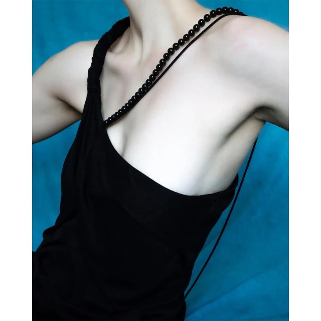 Close-up of a fair-skinned adult female wearing a black dress and black beaded necklace against a turquoise backdrop in a photo studio.